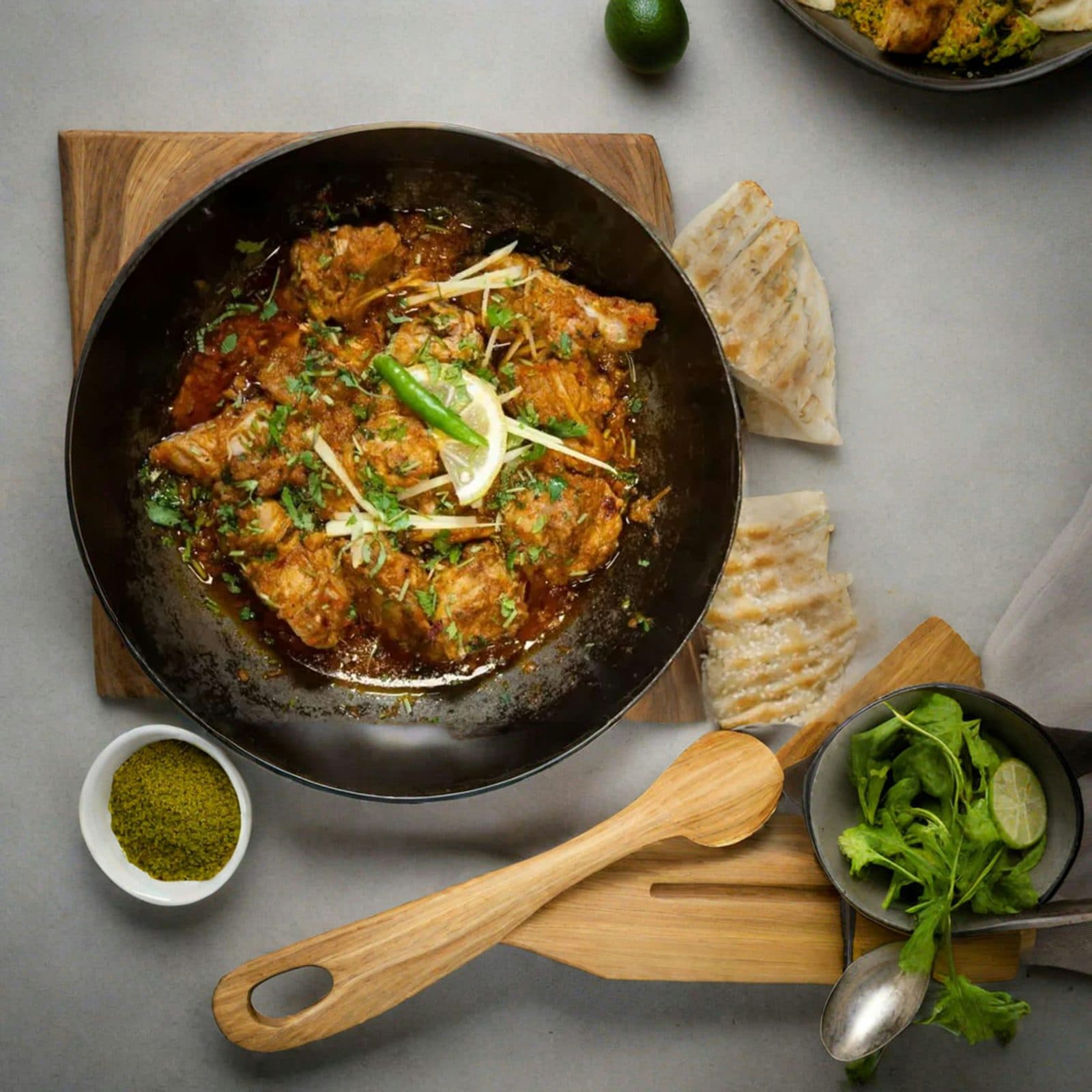Chicken karahi in a black karahi with fresh herbs and naan